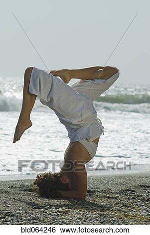Stock Photograph - Hispanic woman doing headstand at beach. Fotosearch