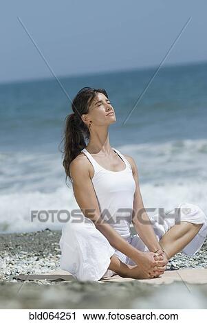 Stock Image - Hispanic woman doing yoga at beach. Fotosearch