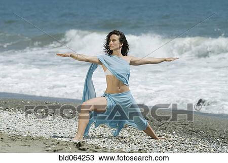 Stock Image - Hispanic woman doing yoga at beach. Fotosearch