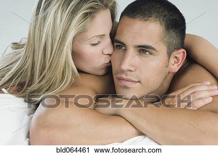 Stock Image - Hispanic woman kissing boyfriend in bed. Fotosearch
