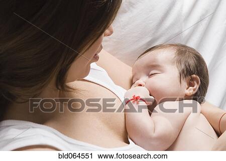 Stock Image - Hispanic woman watching baby sleep. Fotosearch
