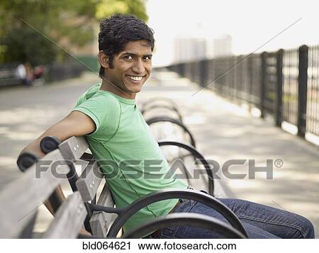 Stock Image - Indian man relaxing on park bench. Fotosearch