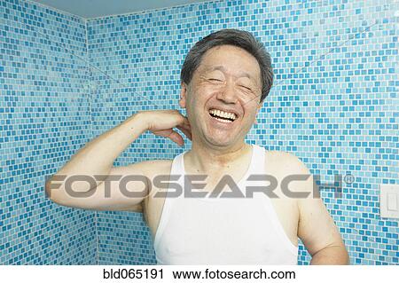 Stock Image - Laughing Asian man in bathroom. Fotosearch