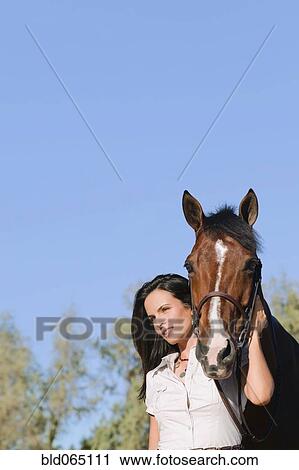 Stock Image - Middle Eastern woman standing with horse. Fotosearch