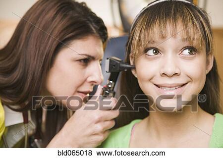 Stock Photo - Mixed race doctor examining teenage girl’s ears. Fotosearch