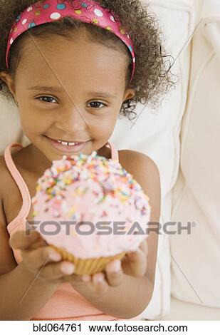 Stock Image - Mixed race girl holding cupcake. Fotosearch