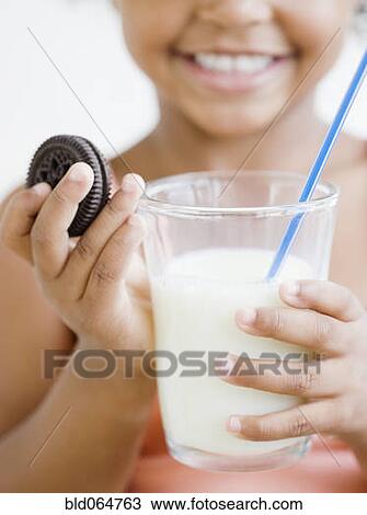 Stock Image - Mixed race girl holding glass of milk and cookie. Fotosearch