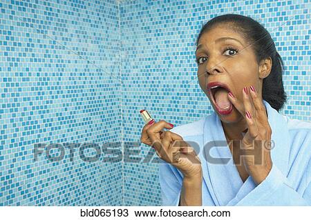 Stock Image - Mixed race woman applying lipstick in bathroom. Fotosearch