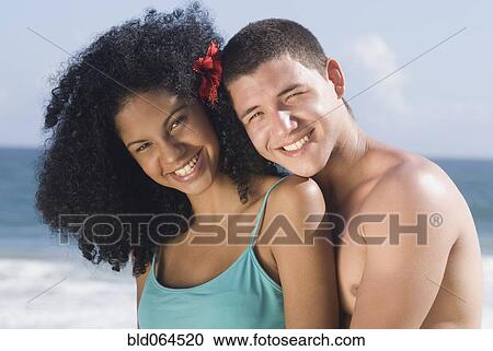 Stock Image - Multi-ethnic couple hugging at beach. Fotosearch