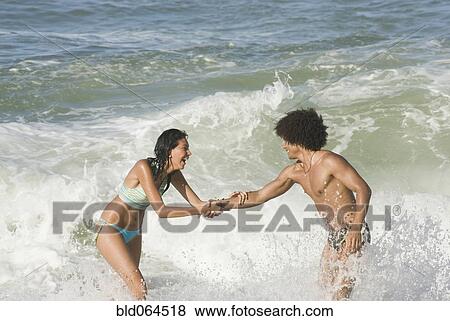 Multi-ethnic couple playing in ocean View Large Photo Image Stock Photo - Multi-ethnic couple playing in ocean. Fotosearch
