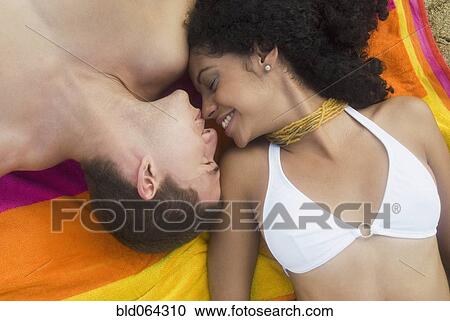 Stock Image - Multi-ethnic couple relaxing at beach. Fotosearch