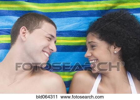 Stock Image - Multi-ethnic couple relaxing at beach. Fotosearch