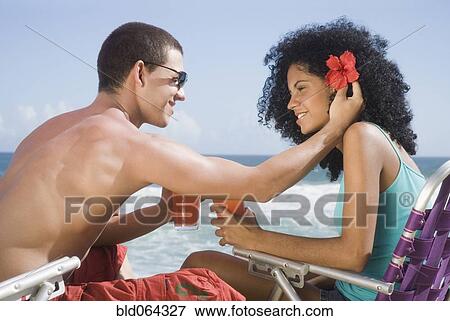 Stock Photo - Multi-ethnic couple relaxing at beach. Fotosearch