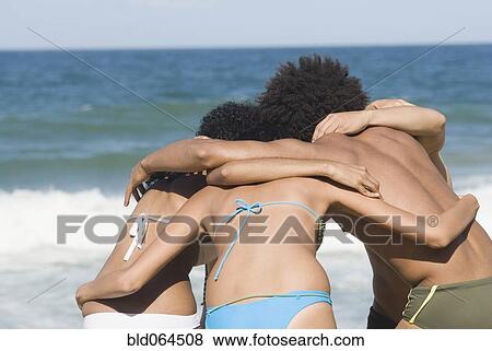 Stock Photo - Multi-ethnic friends hugging on beach. Fotosearch