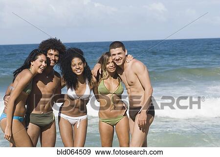 Stock Photo - Multi-ethnic friends hugging on beach. Fotosearch