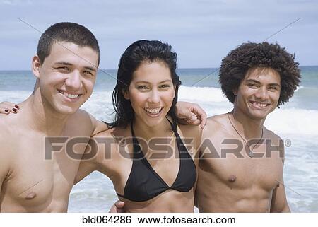 Stock Photograph - Multi-ethnic friends hugging on beach. Fotosearch