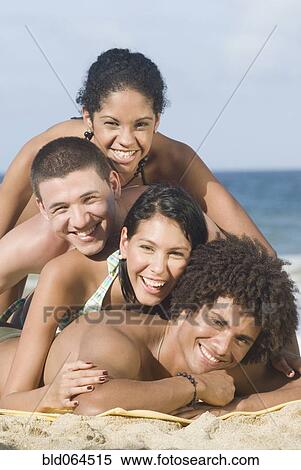 Stock Photography - Multi-ethnic friends laying in pile on beach. Fotosearch