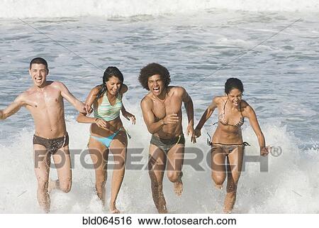 Stock Photograph - Multi-ethnic friends running in surf at beach. Fotosearch