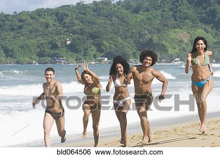 Stock Photograph - Multi-ethnic friends running on beach. Fotosearch
