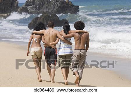 Stock Photograph - Multi-ethnic friends walking on beach. Fotosearch