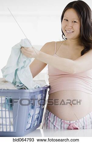 Stock Image - Pregnant Asian woman doing laundry. Fotosearch