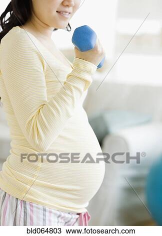 Stock Image - Pregnant Asian woman lifting dumbbells. Fotosearch
