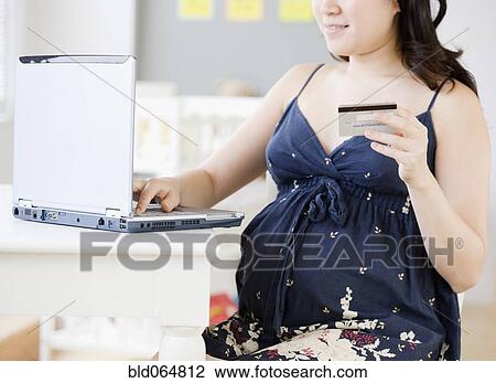 Stock Image - Pregnant Asian woman shopping online with credit card. Fotosearch