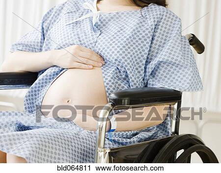 Stock Image - Pregnant Asian woman sitting in wheelchair at hospital. Fotosearch
