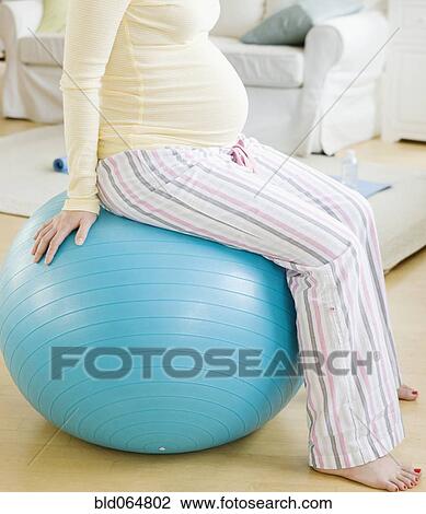Stock Image - Pregnant Asian woman sitting on exercise ball. Fotosearch