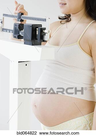 Stock Image - Pregnant Asian woman weighing herself. Fotosearch