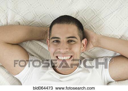 Stock Image - Smiling Hispanic man laying in bed. Fotosearch