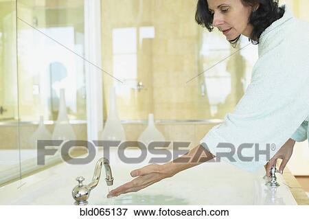 Stock Photo - Smiling Middle Eastern woman checking water temperature in spa. Fotosearch