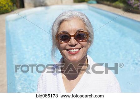 Stock Image - Woman at poolside in bathrobe and sunglasses. Fotosearch