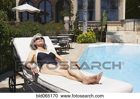 Stock Image - Woman at poolside laying on lounge chair. Fotosearch
