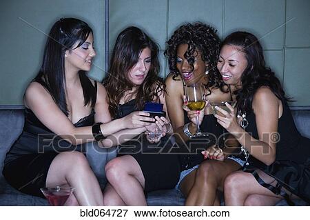 Women in nightclub drinking cocktails and text messaging on cell phone View Large Photo Image Stock Photo - Women in nightclub drinking cocktails and text messaging on cell phone. Fotosearch