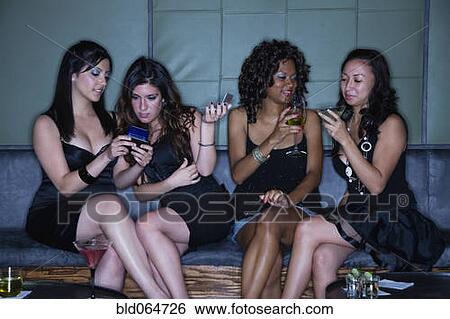 Women in nightclub drinking cocktails and text messaging on cell phone View Large Photo Image Stock Photograph - Women in nightclub drinking cocktails and text messaging on cell phone. Fotosearch