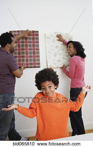 Stock Image - African boy shrugs while parents choose wallpaper. Fotosearch