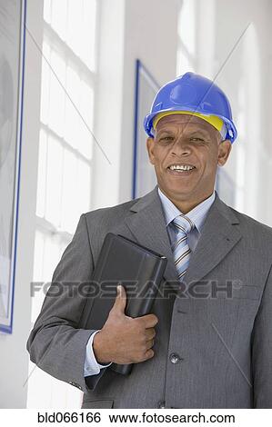 Stock Photograph - African businessman in hard-hat holding binder. Fotosearch