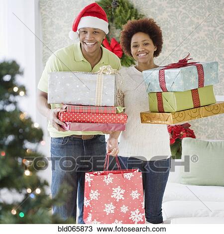 Stock Image - African couple holding stacks of Christmas presents. Fotosearch