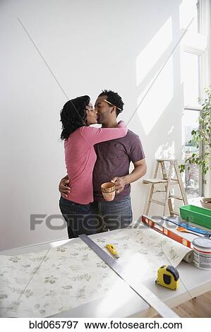 Stock Photo - African couple measuring wallpaper and kissing. Fotosearch