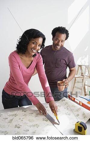 Stock Photograph - African couple measuring wallpaper. Fotosearch