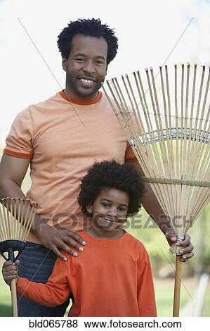 Stock Photo - African father and son holding rakes. Fotosearch