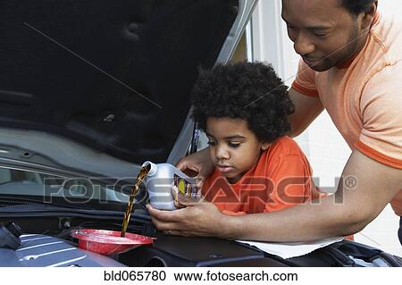 Stock Image - African father helping son pour oil into car engine. Fotosearch