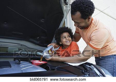 Stock Image - African father helping son pour oil into car engine. Fotosearch
