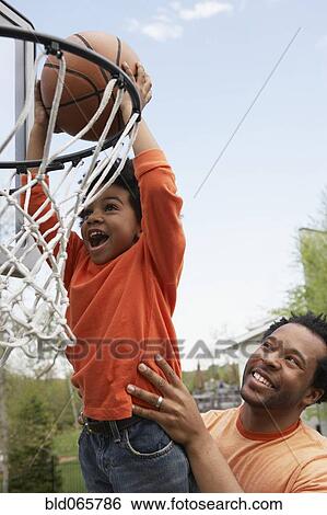Stock Photograph - African father lifting son to basketball hoop. Fotosearch