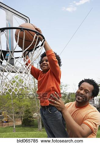 Stock Photography - African father lifting son to basketball hoop. Fotosearch