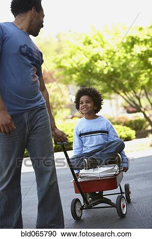 Stock Image - African father pulling son in wagon of recycling. Fotosearch