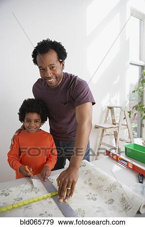 Stock Photo - African father showing son how to measure wallpaper. Fotosearch