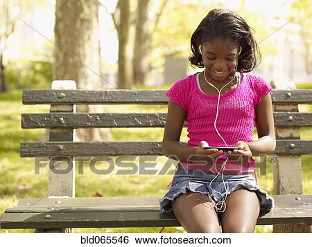 Stock Photograph - African girl listening to mp3 player in park. Fotosearch