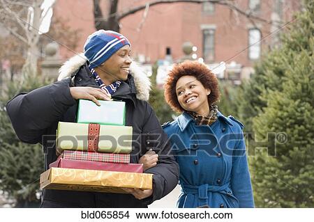 Picture - African man carrying stack of Christmas presents for girlfriend. Fotosearch